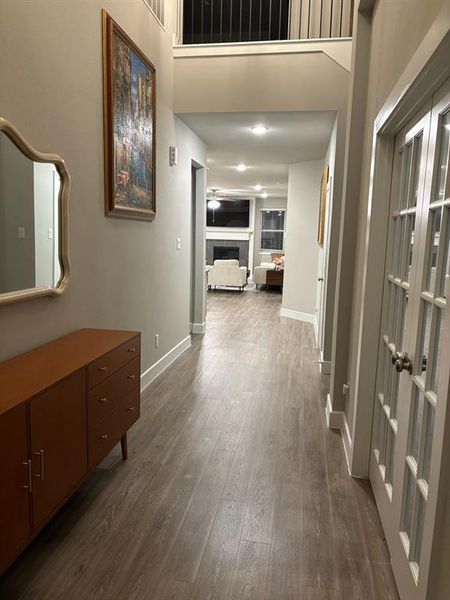 This is a modern well-lit hallway with high ceilings,and neutral wall colors, leading into a cozy, well-lit living area. The flooring is modern laminate, and French doors on the right for an additional room. It's a clean, inviting space that seamlessly connects different areas of the home.