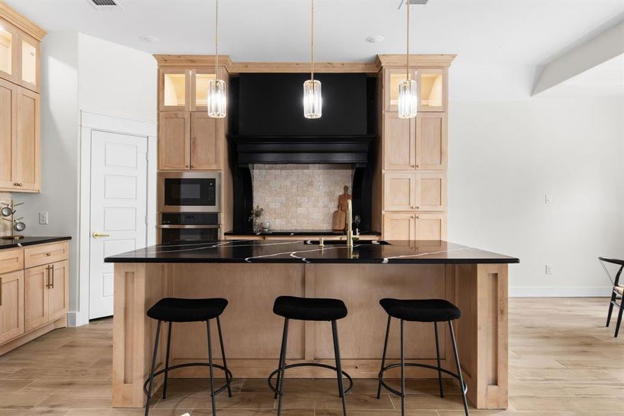 Kitchen featuring light wood-type flooring, hanging light fixtures, stainless steel oven, built in microwave, and a center island with sink