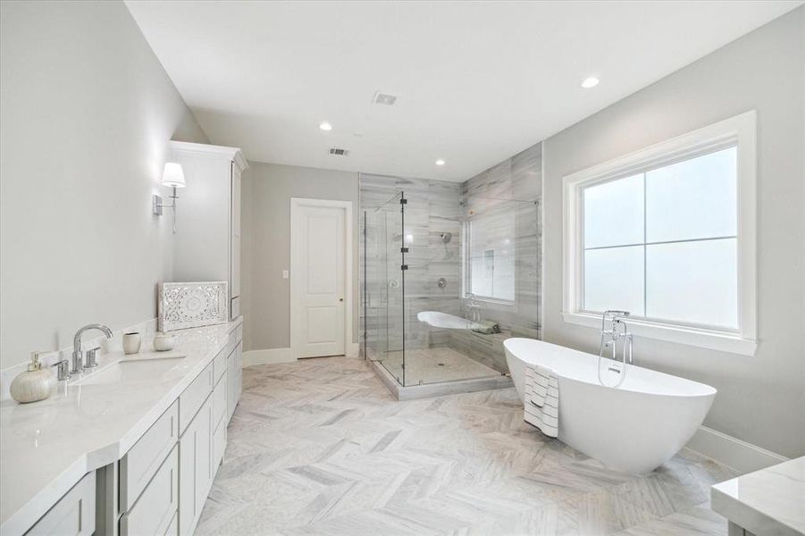 Elegant bathroom featuring a freestanding tub, a spacious glass-enclosed shower, dual vanity with ample storage, and herringbone tile flooring, all bathed in natural light from a large window.