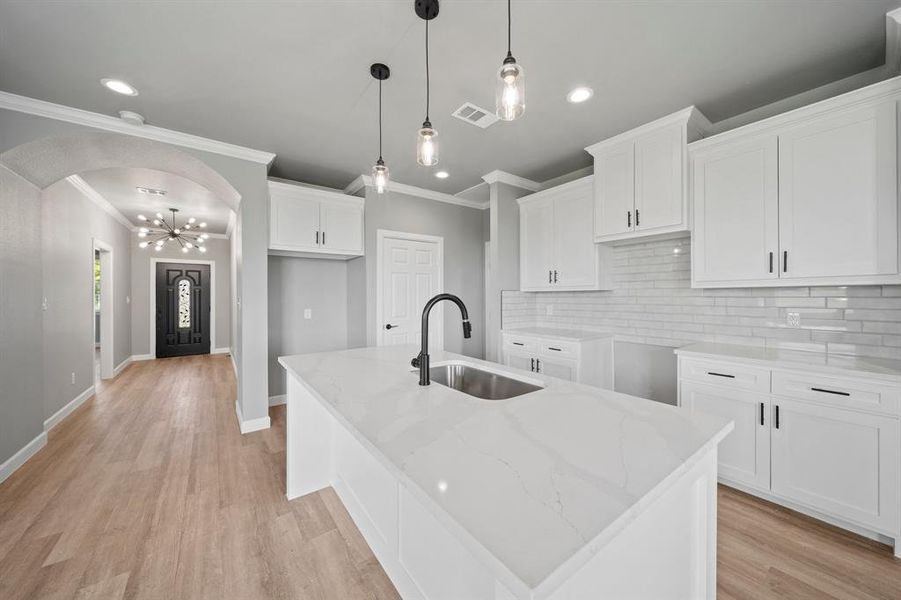 Kitchen with white cabinetry, tasteful backsplash, crown molding, light stone counters, and light hardwood / wood-style flooring