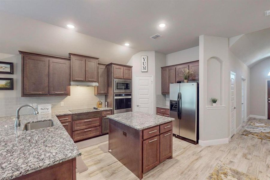 Kitchen featuring tasteful backsplash, stainless steel appliances, sink, a kitchen island, and light wood-type flooring