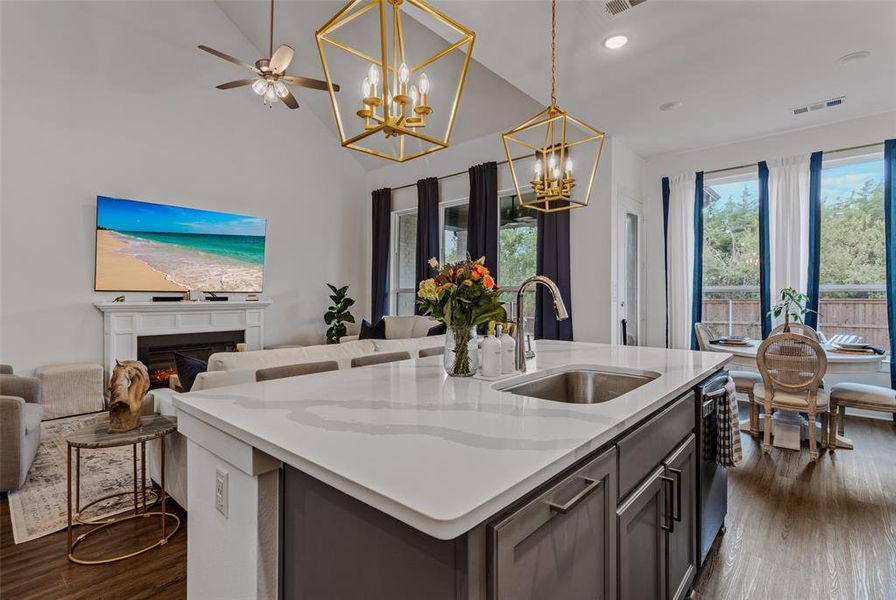 Kitchen featuring dark hardwood / wood-style floors, hanging light fixtures, a center island with sink, sink, and light stone counters