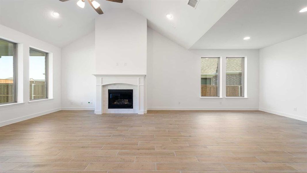 Unfurnished living room with high vaulted ceiling, a tiled fireplace, light hardwood / wood-style floors, and ceiling fan