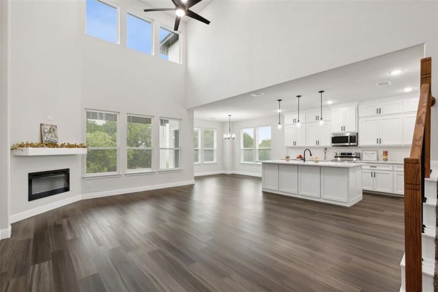 Unfurnished living room featuring dark wood-type flooring, sink, ceiling fan with notable chandelier, and a towering ceiling