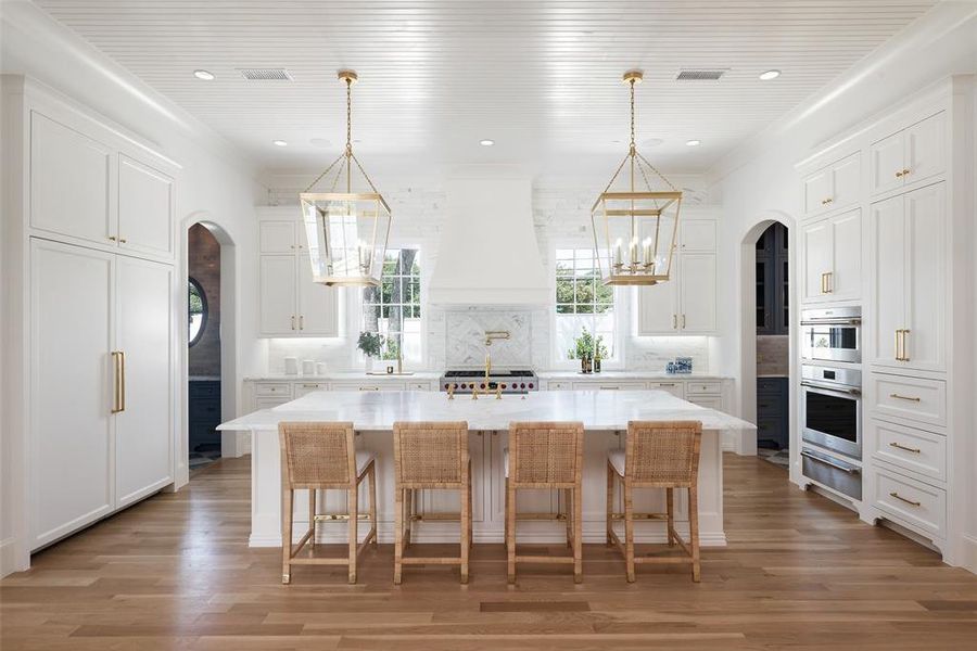 Kitchen featuring custom exhaust hood, decorative backsplash, light wood-flooring, and a kitchen island