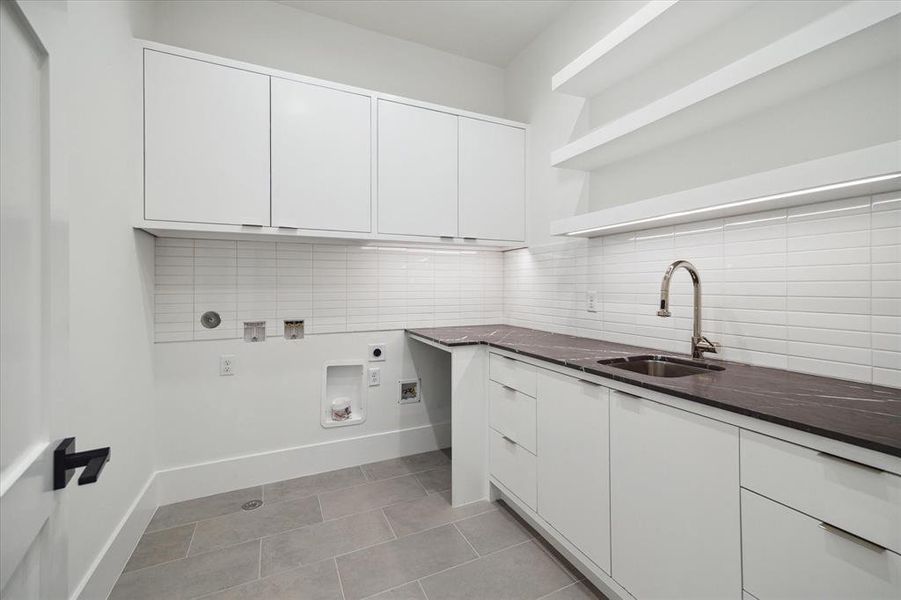 The oversized utility room blends style and functionality seamlessly with its tile flooring, built-in cabinetry, and polished nickel Emtek tab pull cabinet hardware. Floating backlit shelves and marble countertops add a touch of sophistication, while the arctic white rectangle tile backsplash completes the elegant look.