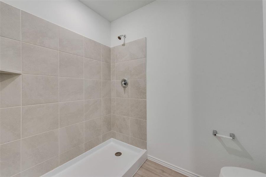 Bathroom with a tile shower, hardwood / wood-style flooring, and toilet