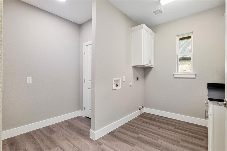 Clothes washing area with electric dryer hookup, cabinets, light wood-type flooring, and hookup for a gas dryer