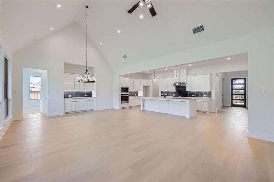 Unfurnished living room featuring light wood-type flooring, high vaulted ceiling, plenty of natural light, and ceiling fan with notable chandelier