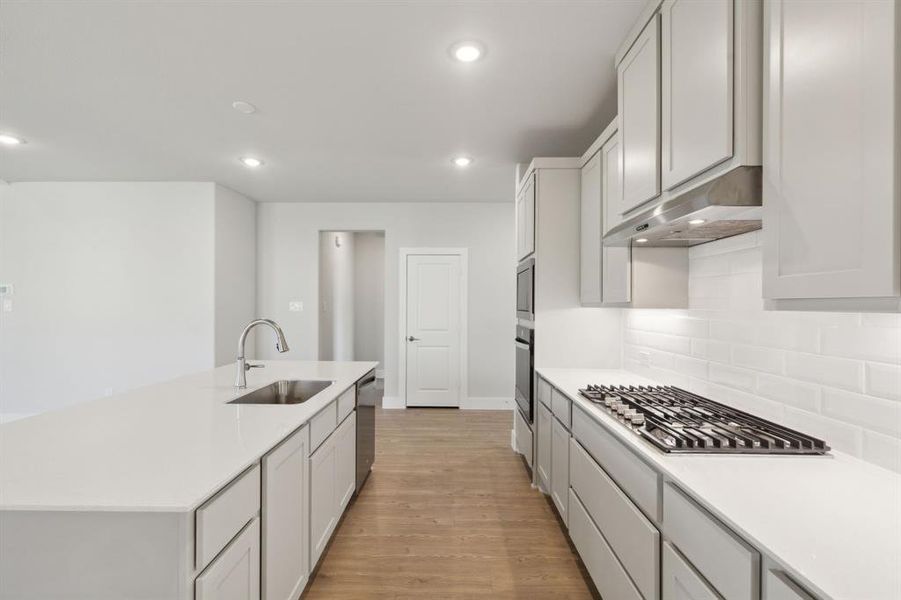 Kitchen featuring appliances with stainless steel finishes, light hardwood / wood-style floors, sink, a center island with sink, and tasteful backsplash