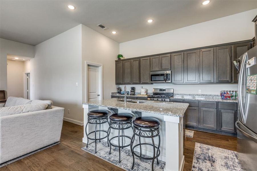 Kitchen with light stone countertops, dark hardwood / wood-style flooring, stainless steel appliances, a kitchen island with sink, and sink