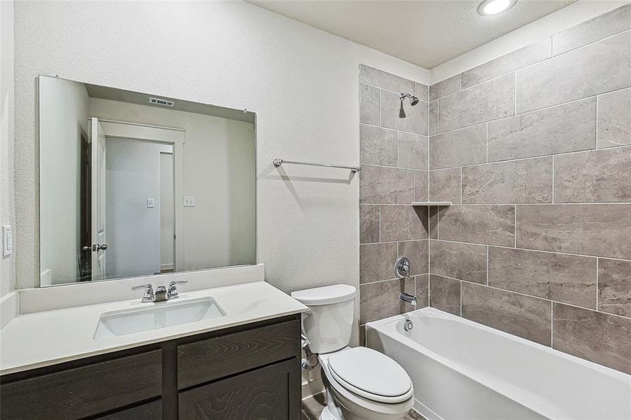 Full bathroom featuring tiled shower / bath, vanity, toilet, and a textured ceiling