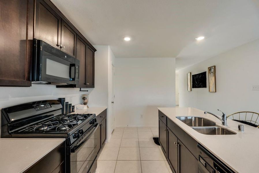 Kitchen featuring black appliances, light tile patterned floors, dark brown cabinetry, and sink