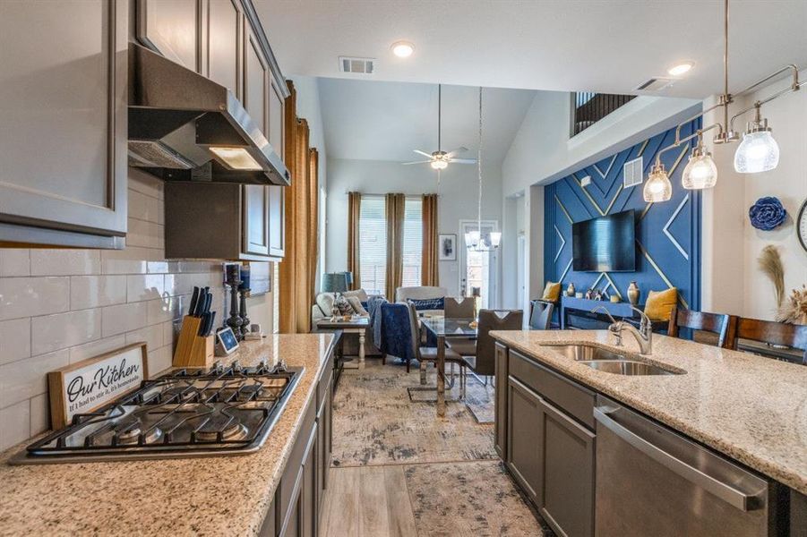 Kitchen with light stone counters, sink, vaulted ceiling, appliances with stainless steel finishes, and decorative light fixtures