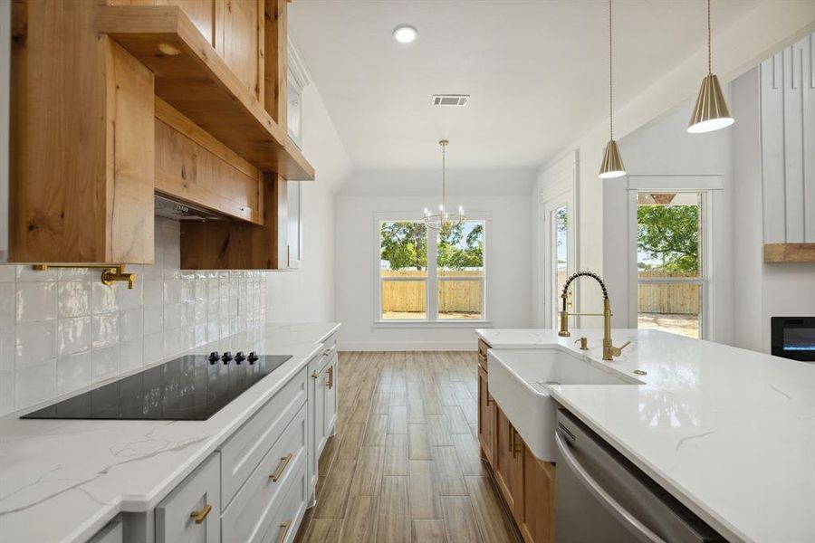 Kitchen with black electric stovetop, light stone countertops, dishwasher, and white cabinets