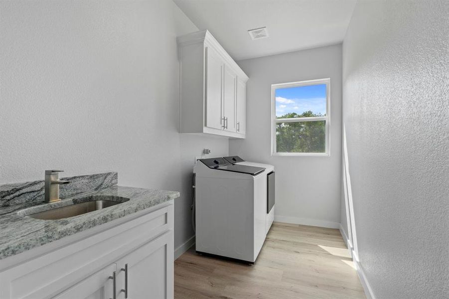 Clothes washing area featuring washing machine and clothes dryer, light hardwood / wood-style floors, cabinets, and sink