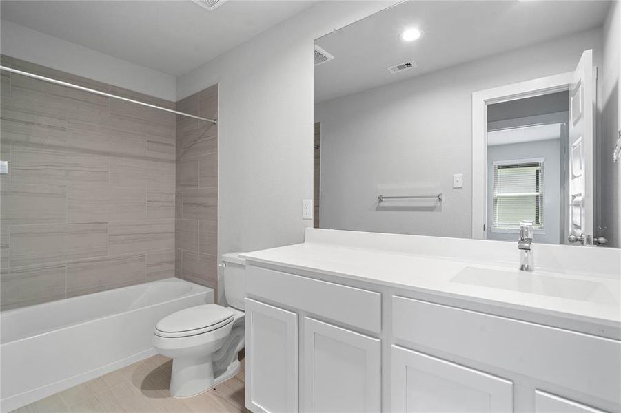 Secondary bath features tile flooring, bath/shower combo with tile surround, stained wood cabinets, beautiful light countertops, mirror, sleek fixtures and modern finishes.