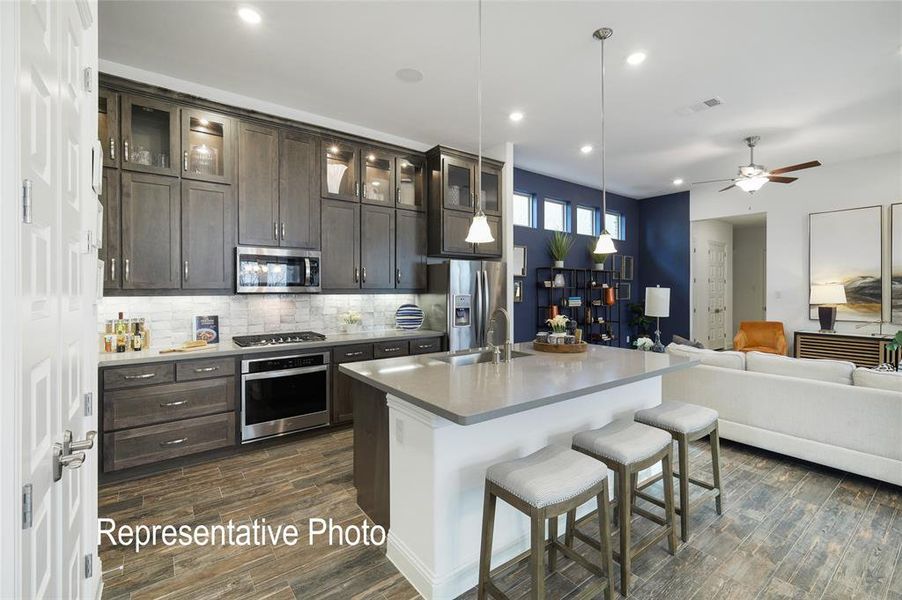 Kitchen with dark brown cabinetry, dark hardwood / wood-style flooring, stainless steel appliances, a center island with sink, and ceiling fan