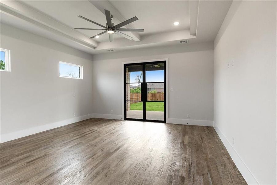 Unfurnished room featuring a wealth of natural light, ceiling fan, hardwood / wood-style flooring, and a tray ceiling