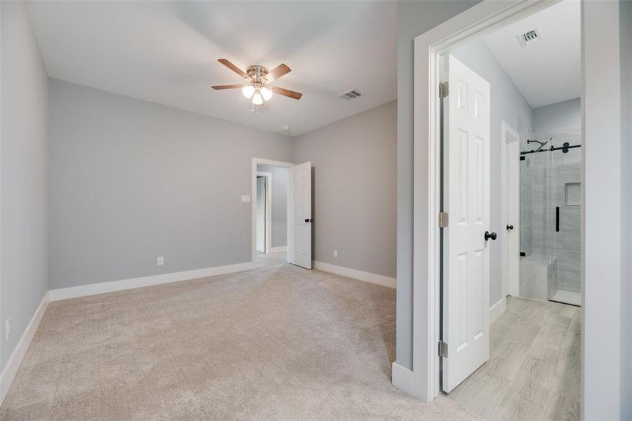 Unfurnished bedroom featuring ensuite bathroom, light colored carpet, and ceiling fan