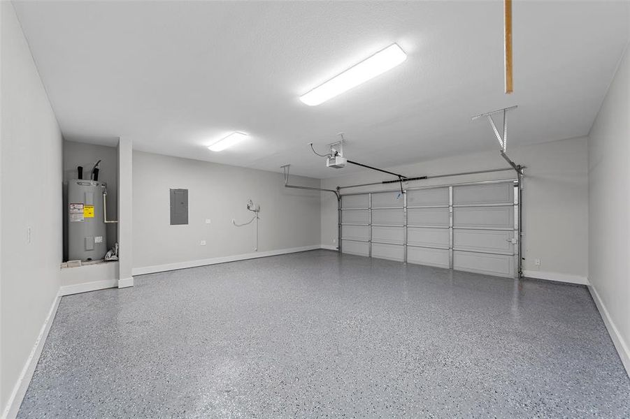 Garage with electric water heater, electric panel, and a garage door opener and epoxy floors