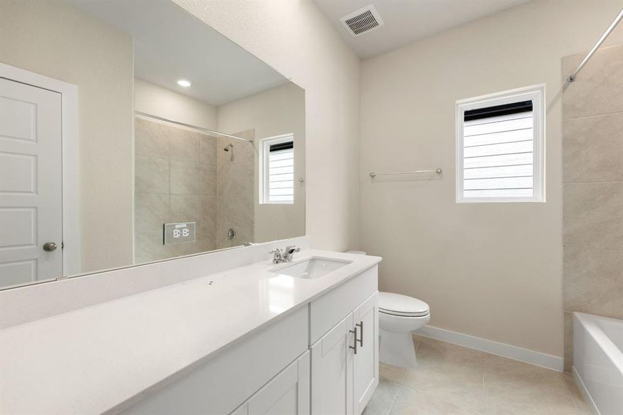 Secondary bathroom features Quartz countertops and bright cabinets, neutral paint, shower/tub combo with tile surround, large mirror, tile floors, sleek fixtures and modern finishes, plenty of space to accommodate any visiting family or guests.