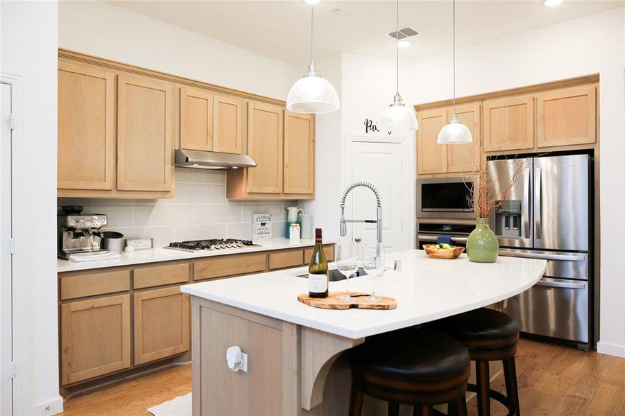 Kitchen featuring decorative backsplash, appliances with stainless steel finishes, light hardwood / wood-style flooring, and a center island with sink