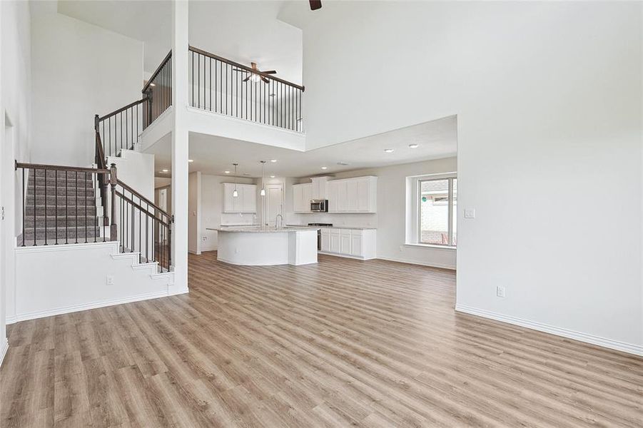 Unfurnished living room featuring sink, ceiling fan, light hardwood / wood-style floors, and a towering ceiling