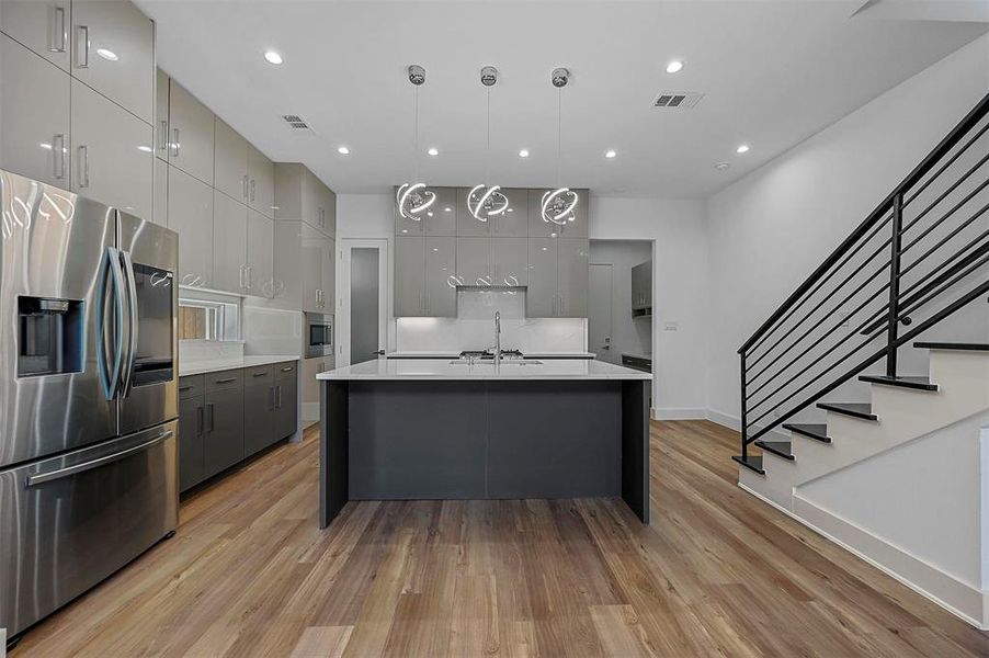 Kitchen with hanging light fixtures, gray cabinets, appliances with stainless steel finishes, and light wood-type flooring