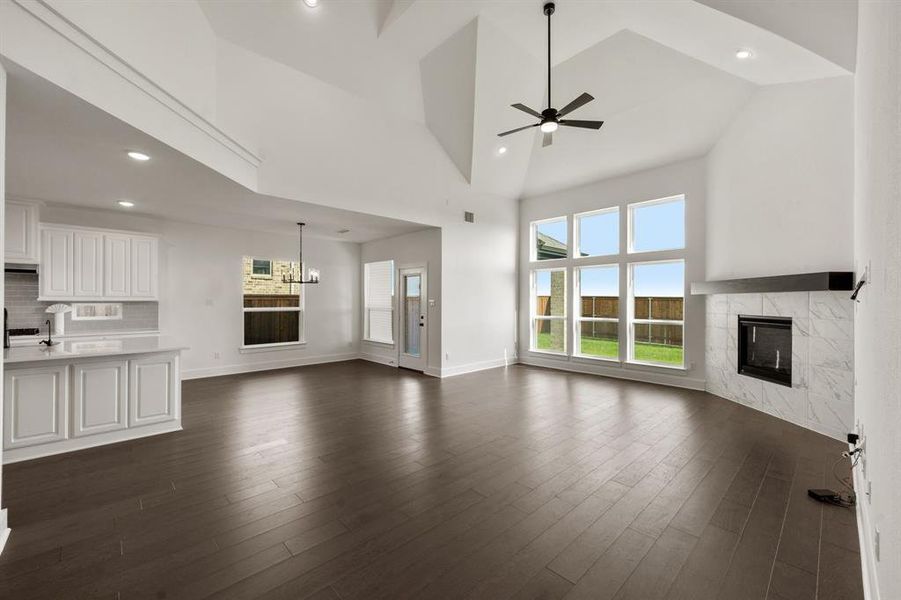 Unfurnished living room with high vaulted ceiling, ceiling fan with notable chandelier, a tiled fireplace, and dark hardwood / wood-style floors