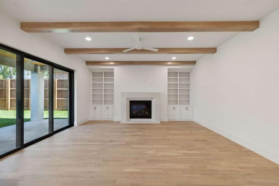 Unfurnished living room featuring ceiling fan, light wood-type flooring, beam ceiling, and built in shelves