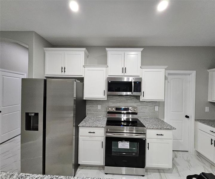 Kitchen featuring white cabinets, appliances with stainless steel finishes, and light stone countertops