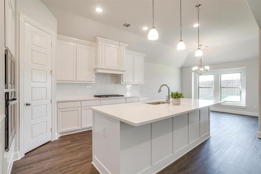 Kitchen featuring a kitchen island with sink, sink, white cabinets, hanging light fixtures, and dark hardwood / wood-style flooring