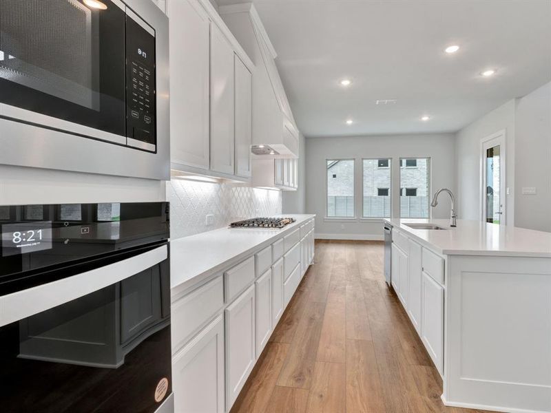 Kitchen with appliances with stainless steel finishes, sink, light hardwood / wood-style floors, a kitchen island with sink, and decorative backsplash