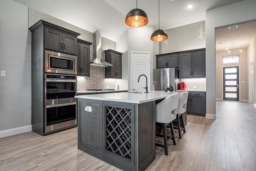 Kitchen featuring backsplash, light hardwood / wood-style floors, appliances with stainless steel finishes, and wall chimney exhaust hood