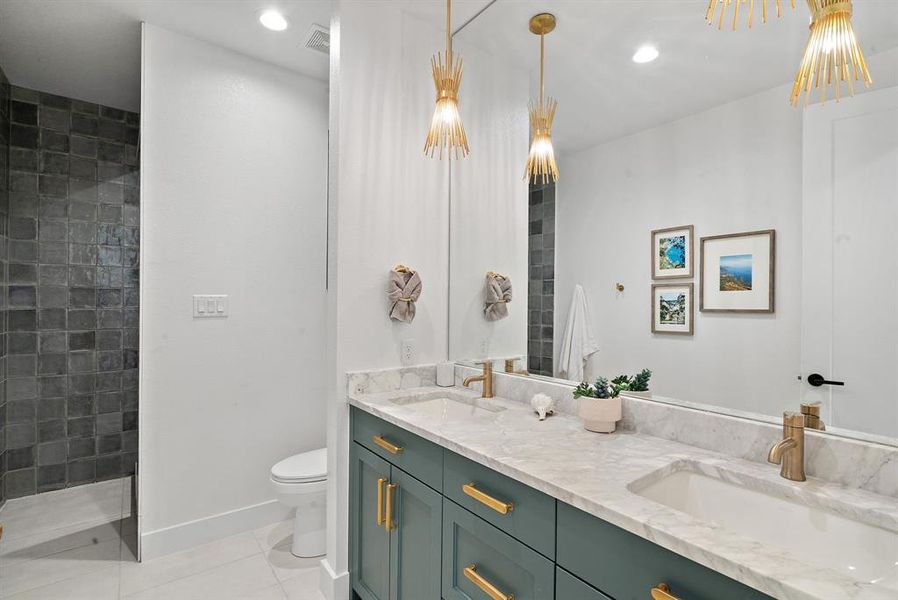 Bathroom featuring toilet, a tile shower, tile patterned flooring, and double vanity