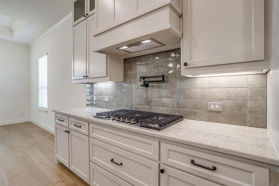 Kitchen with white cabinetry, premium range hood, light wood-type flooring, ornamental molding, and backsplash