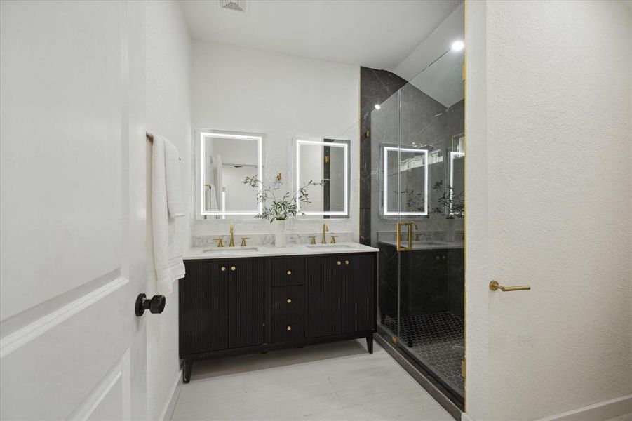 The primary ensuite bathroom exudes luxury with its furniture-style vanity and lit mirrors. Indulge in the spacious walk-in shower, with frameless glass, modern hardware, and exquisite tile work. This elegant space seamlessly blends style and functionality, creating the perfect retreat.
