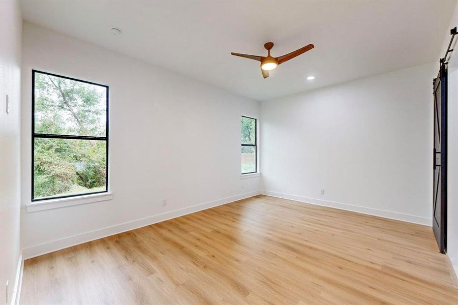 Empty room featuring ceiling fan, a barn door, and light hardwood / wood-style floors