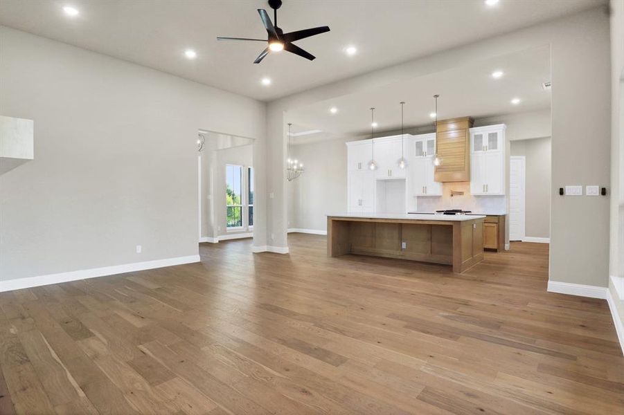 Kitchen with white cabinets, hanging light fixtures, a spacious island, ceiling fan with notable chandelier, and hardwood / wood-style floors