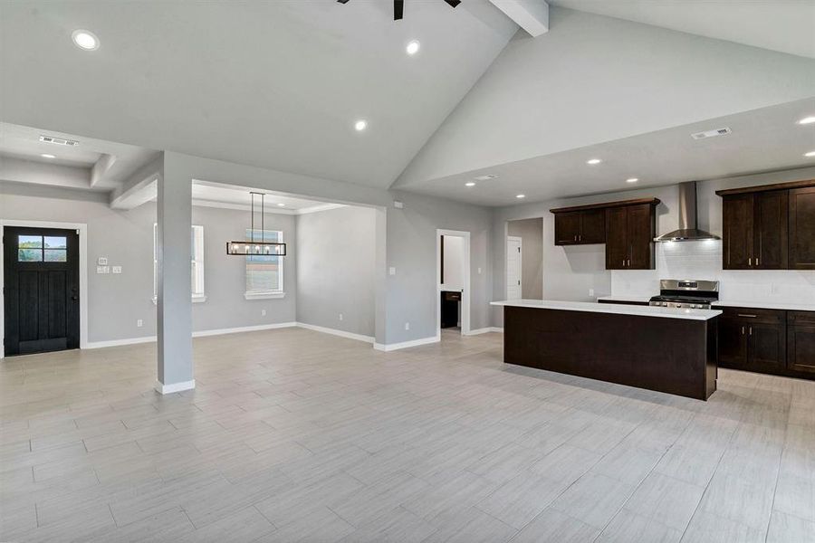 Kitchen with high vaulted ceiling, wall chimney exhaust hood, a kitchen island, stainless steel gas range, and a notable chandelier