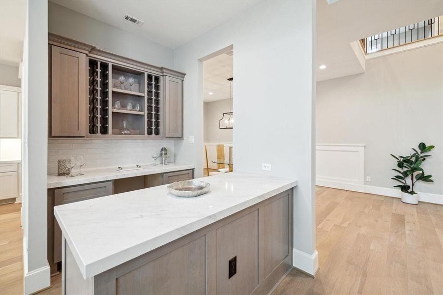 This beautiful wet bar is nestled between the kitchen and dining room.   a modern, open-concept space featuring a kitchen with a large island, marble countertops, built-in wine rack with Benedetinni cabinetry throughout the house.