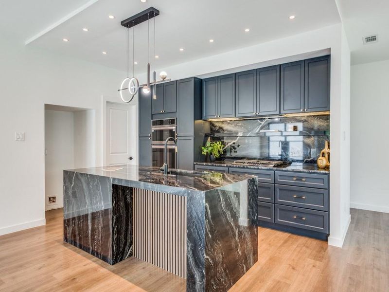 Kitchen with pendant lighting, a large island with sink, sink, light hardwood / wood-style flooring, and dark stone countertops