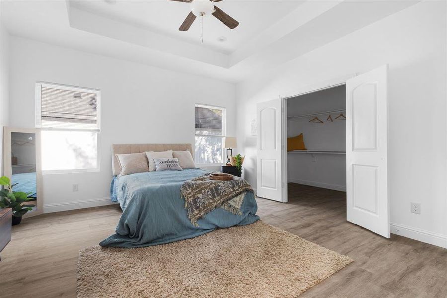 Bedroom with multiple windows, wood-type flooring, a raised ceiling, and ceiling fan