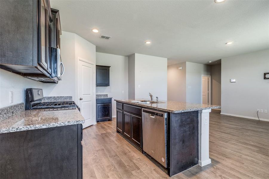 Kitchen featuring light hardwood / wood-style floors, appliances with stainless steel finishes, and an island with sink
