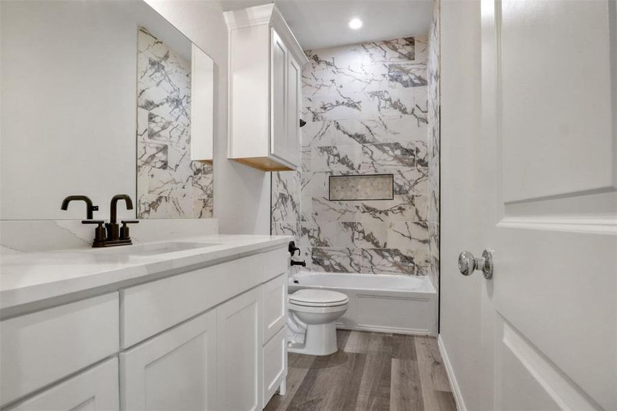 Full bathroom with wood-type flooring, tiled shower / bath, vanity, and toilet