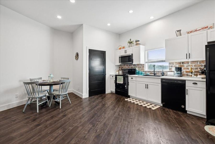 Kitchen featuring white cabinets, sink, decorative backsplash, dark hardwood / wood-style flooring, and black appliances