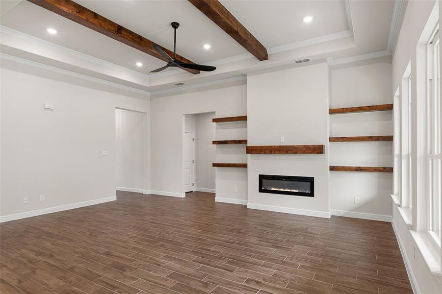 Unfurnished living room featuring beam ceiling, dark wood-type flooring, crown molding, and ceiling fan