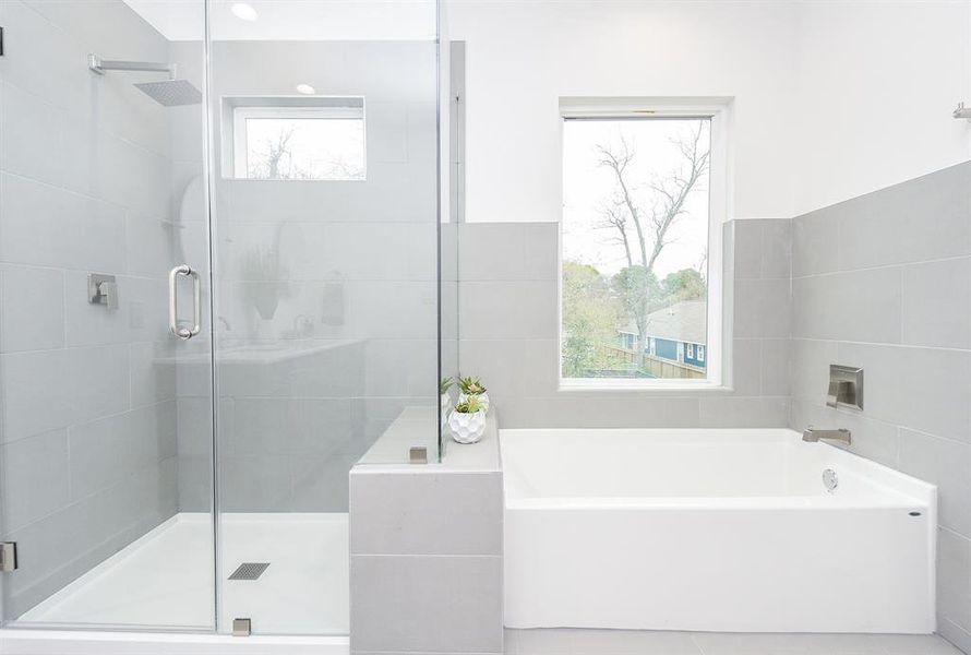 Simplicity equals elegance in your primary ensuite bathroom; with rimless walk-in, glass enclosed shower, sitting right next to a welcoming tub, under a clear paned window.