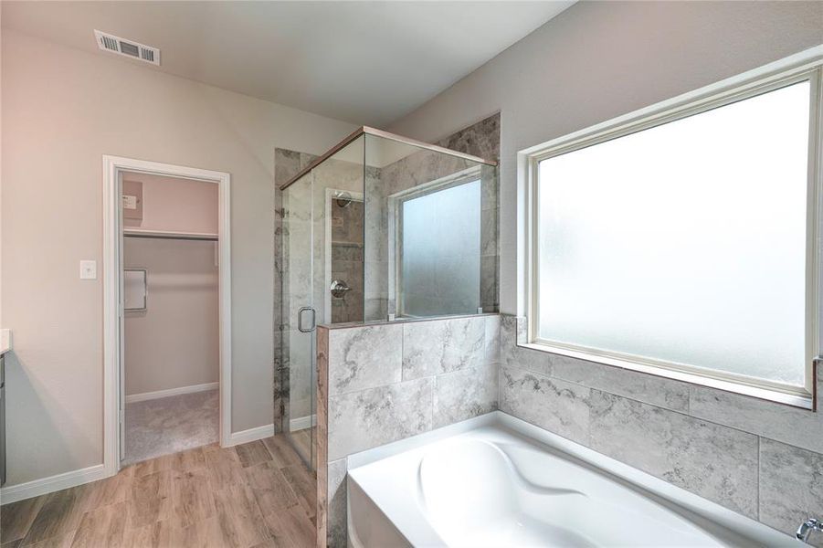 This bathroom boasts modern finishes, including a walk-in shower, a large soaking tub, and a built-in closet for storage. Natural light streams in through a frosted window, providing both illumination and privacy.